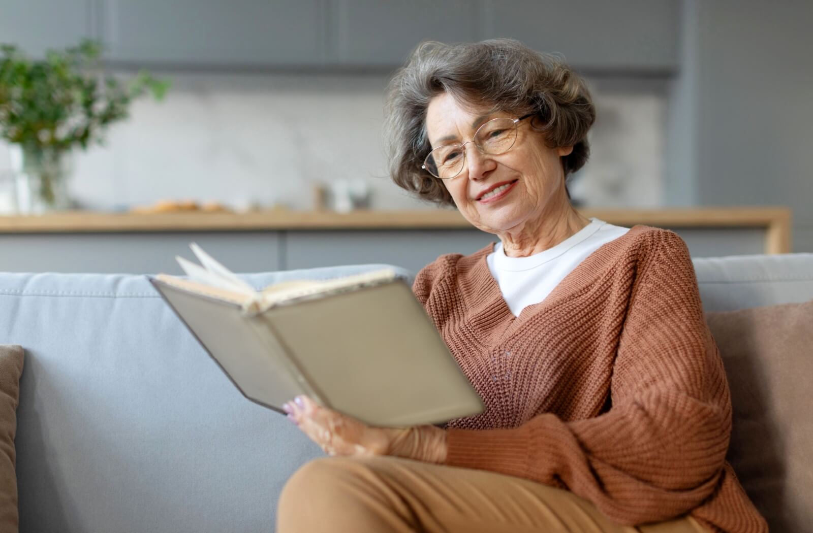 A happy older adult reads a book to discuss in their senior book club.