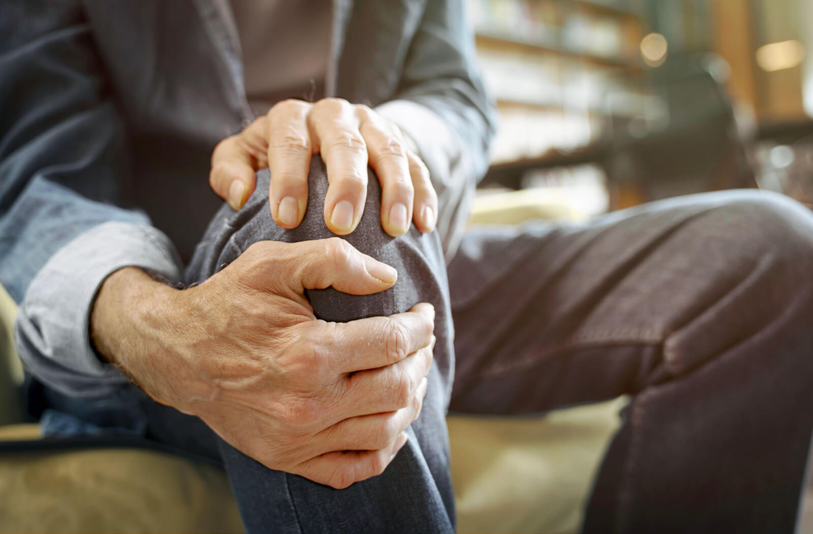 A close-up image of an older adult rubbing their right knee in frustration due to joint pain.