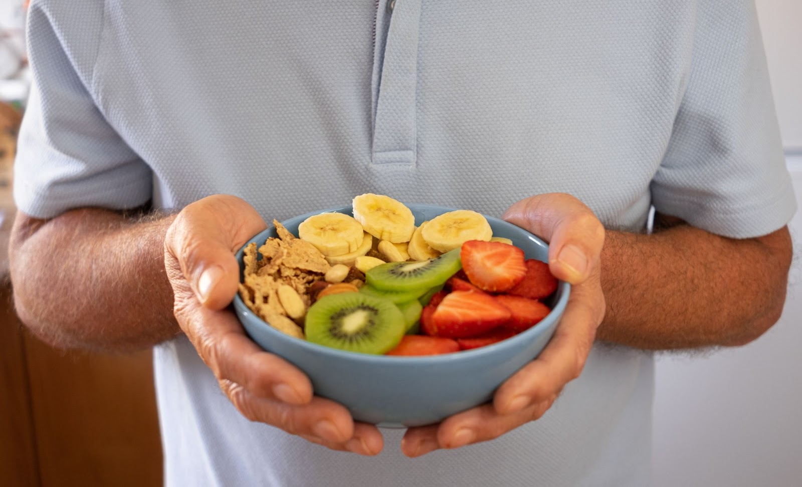 A close-up of an older adult holding a bowl with both hands filled with colorful fruits.