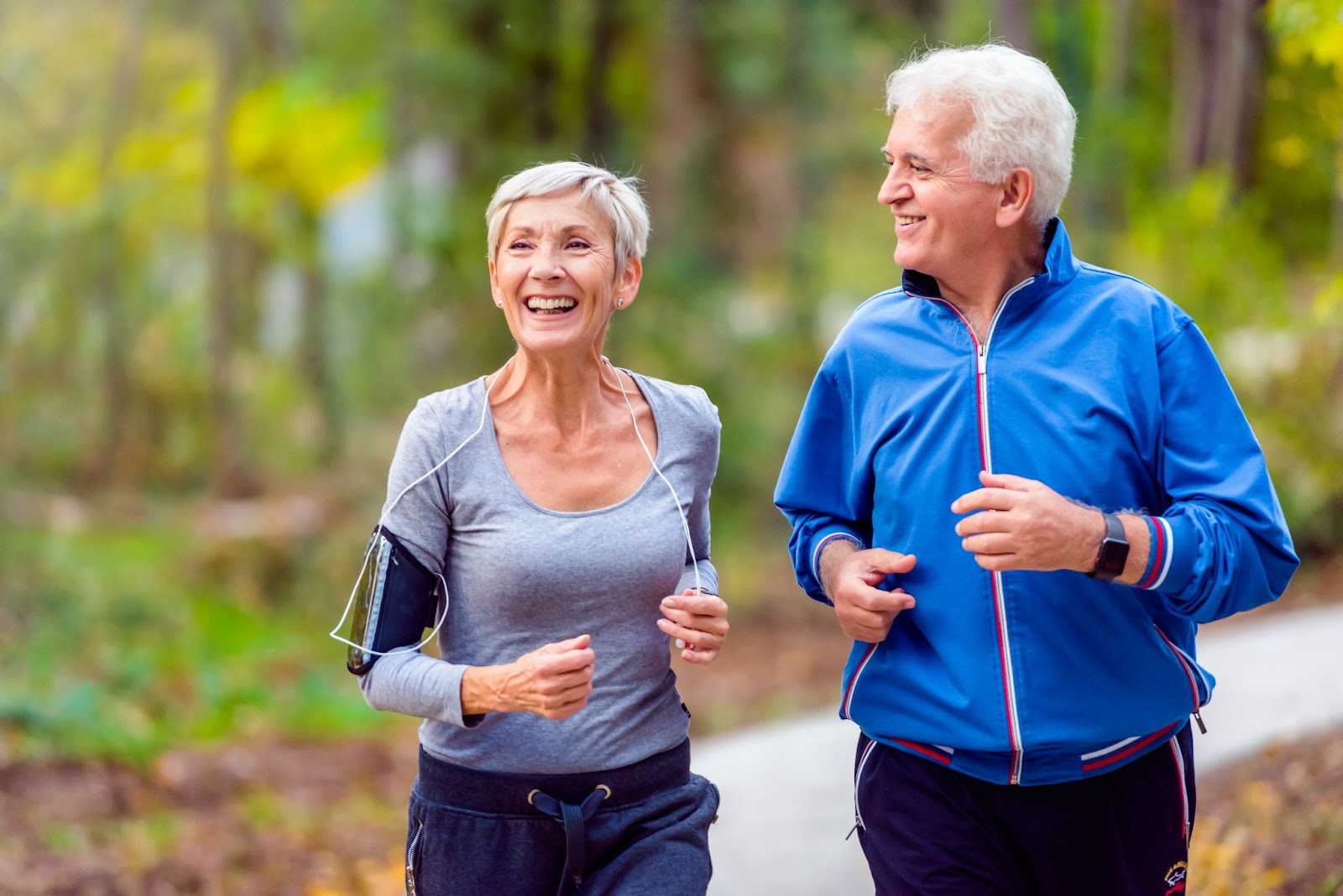 An elderly couple smiling and jogging outdoors.