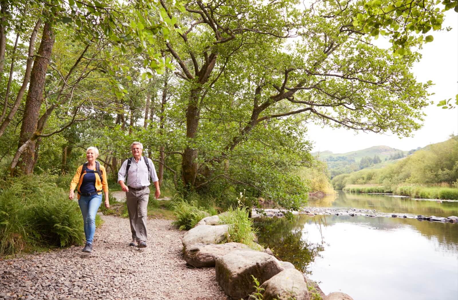 A senior couple, well prepared with backpacks, hike in a state park near a river to enjoy nature and get exercise