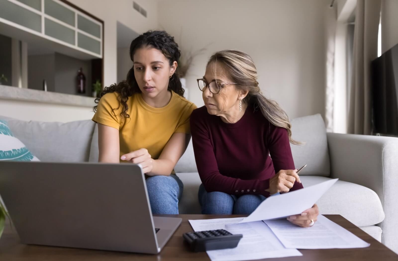 An adult child helps their older parent sort through paperwork while researching senior living options together on the couch
