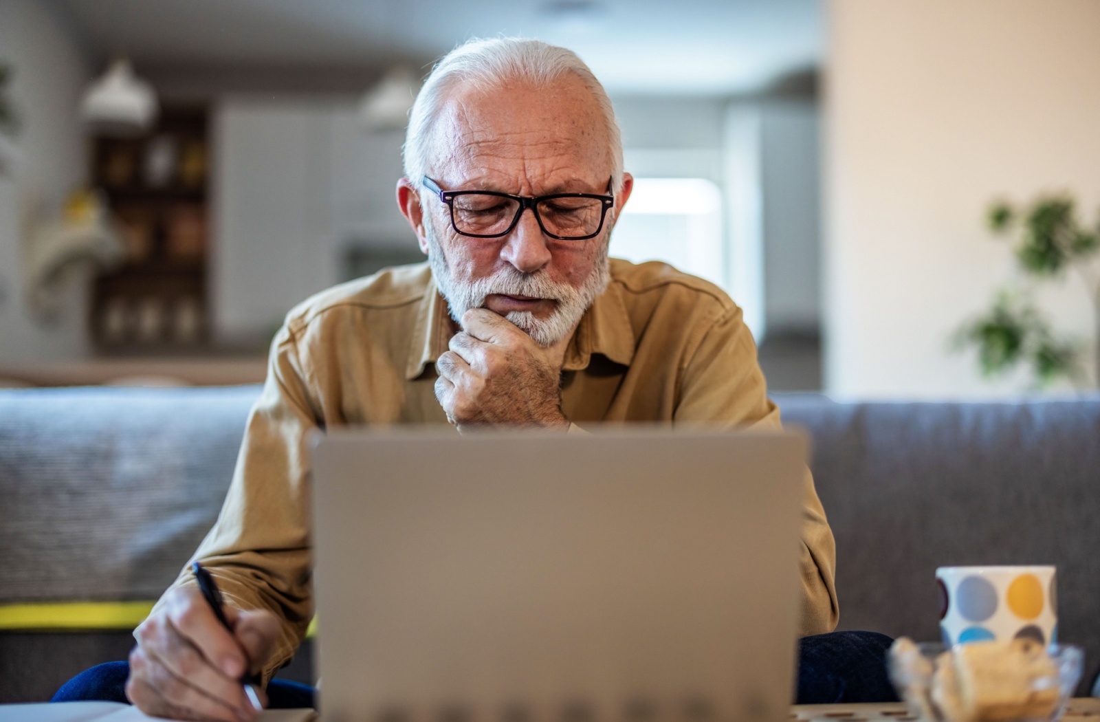 An older adult thoughtfully looks at their computer while planning for their retirement in their living room