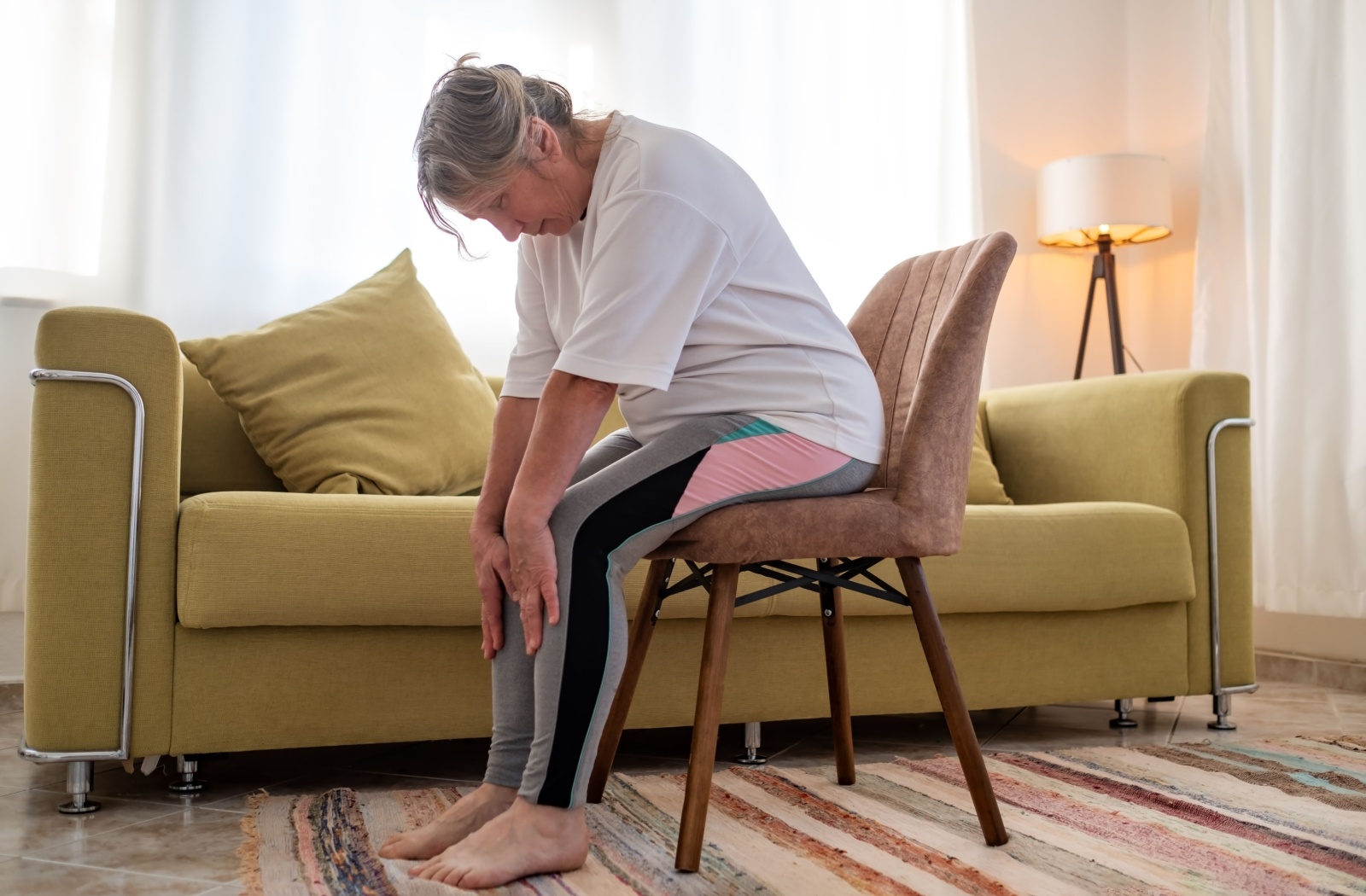 A senior sits on a chair and stretches their back, helping to improve their posture.